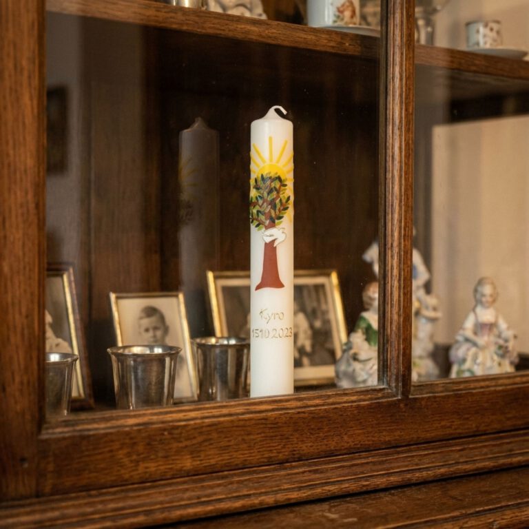 Taufkerze steht geschützt in einer Vitrine neben alten Familienfotos und Erinnerungsstücken.